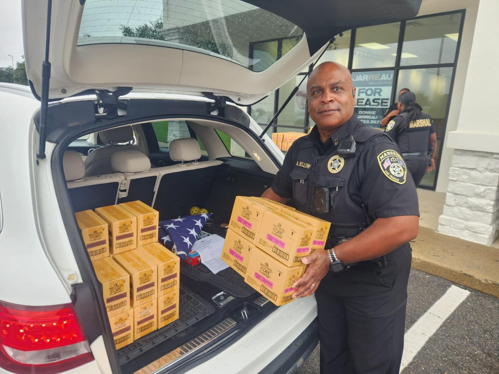 A Marshal Deputy is loading boxes of cat food into the back of a car.