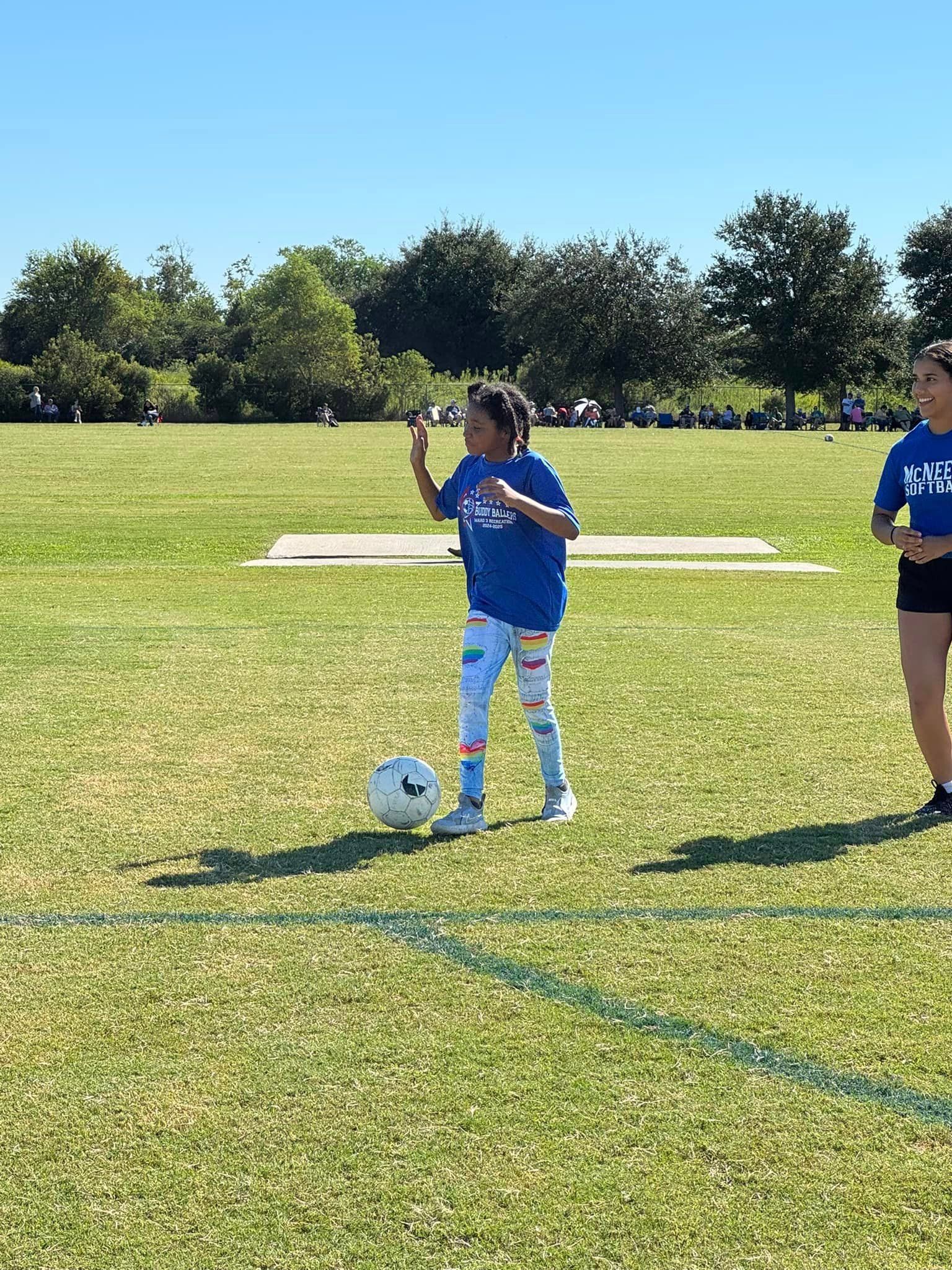 A girl in a blue shirt is kicking a soccer ball on a field.