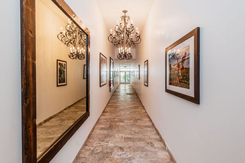 A long hallway with two mirrors on the wall and a chandelier hanging from the ceiling.