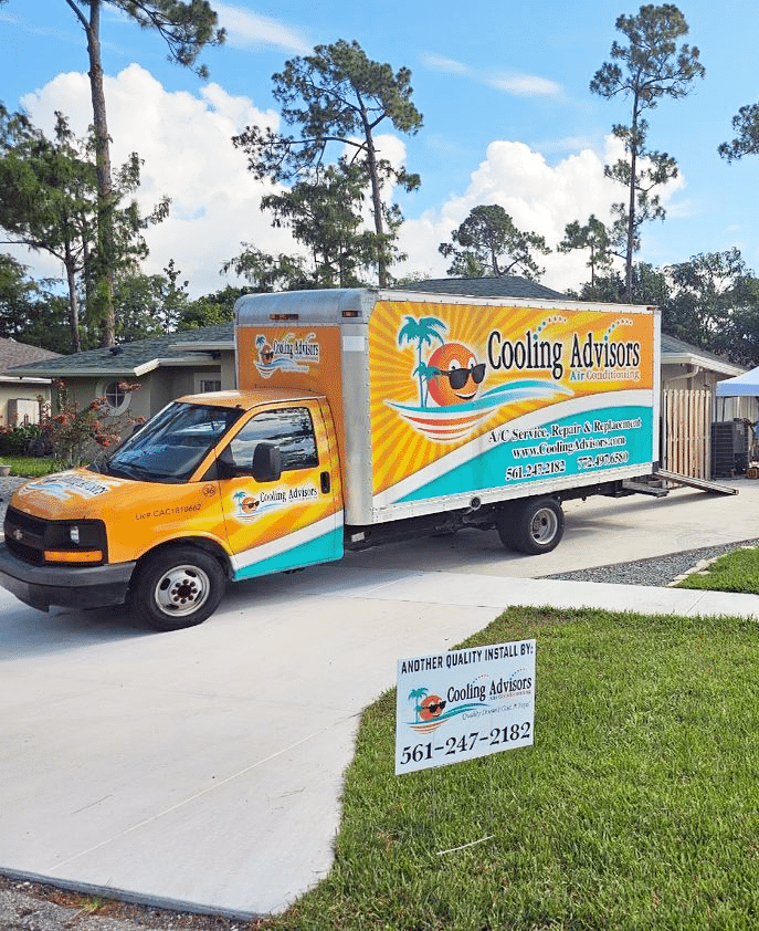 Orange and turquoise Cooling Tans delivery truck parked on a driveway beside a lawn sign.
