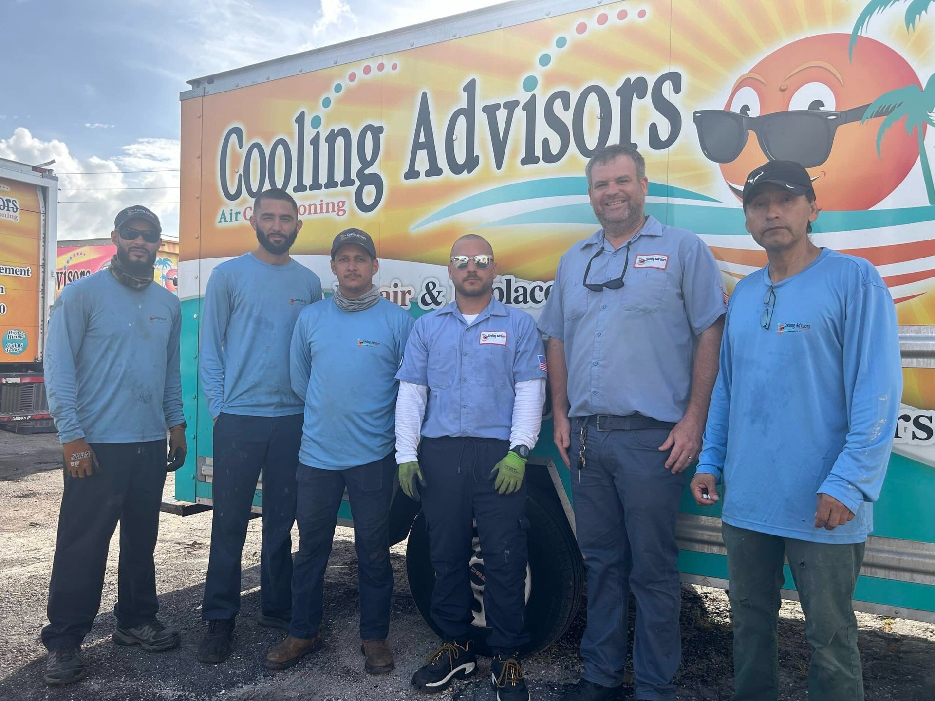 Group of six men in blue shirts standing in front of a truck with