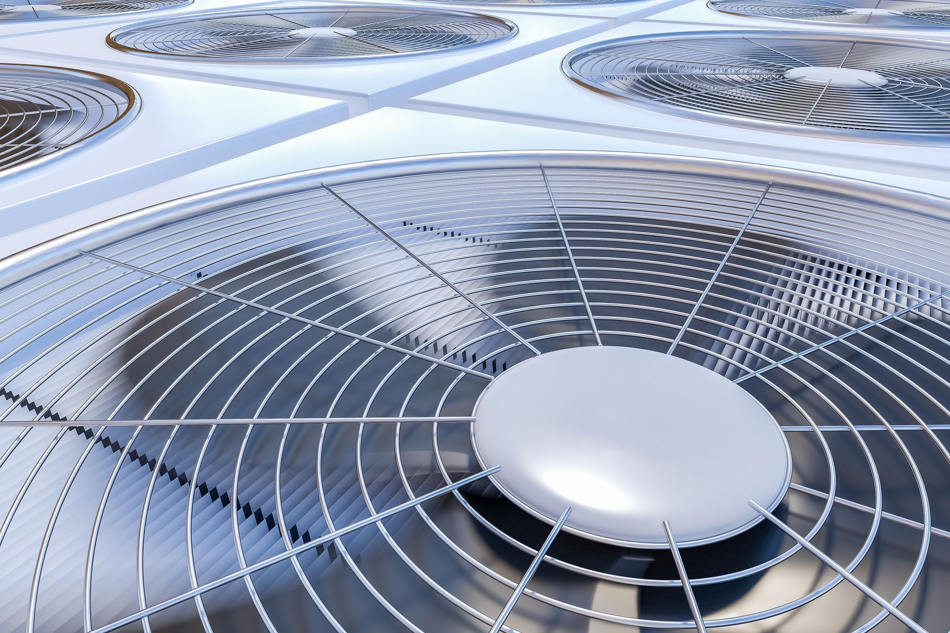 Close-up of numerous air conditioning units, metal fan grilles and silver housing, outdoors.