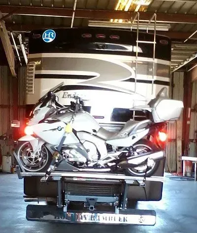 Motorcycle mounted on a carrier attached to the back of a recreational vehicle.