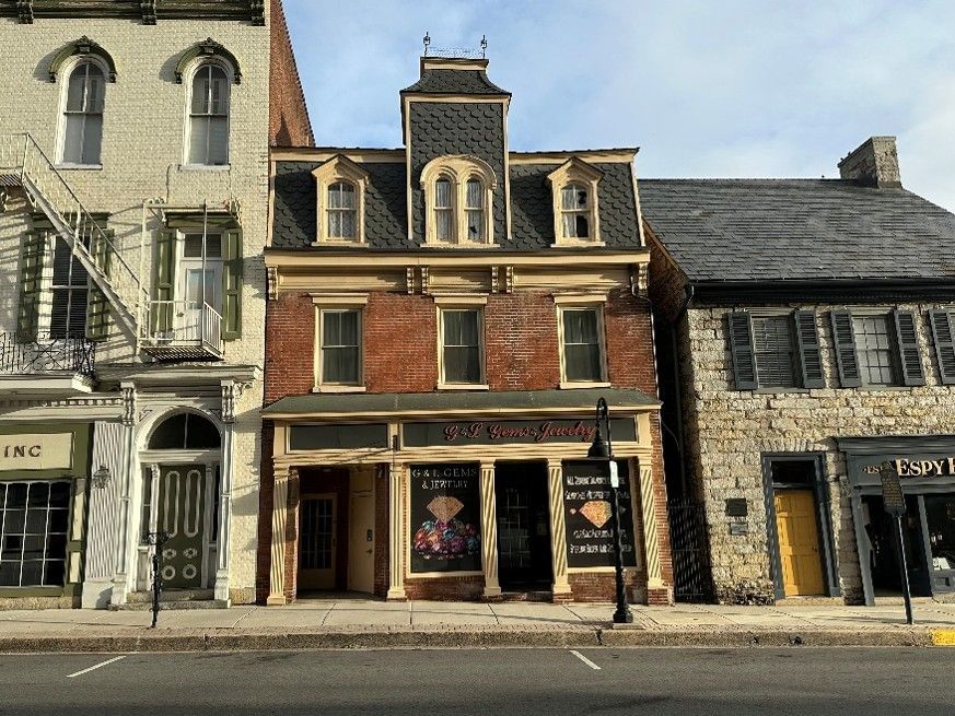 Three historic storefronts on a street, with a central red-brick building and adjacent stone and dark wood facades.