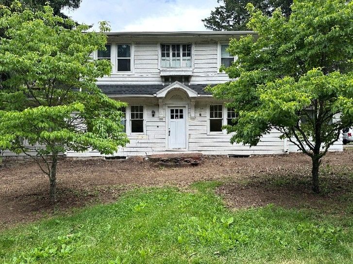 White two-story house with black shutters and front porch, framed by green trees and lawn