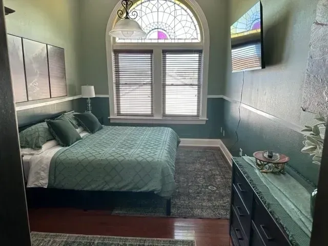 Bedroom with teal bed, arched window, gray rug, and dark dresser against mint walls
