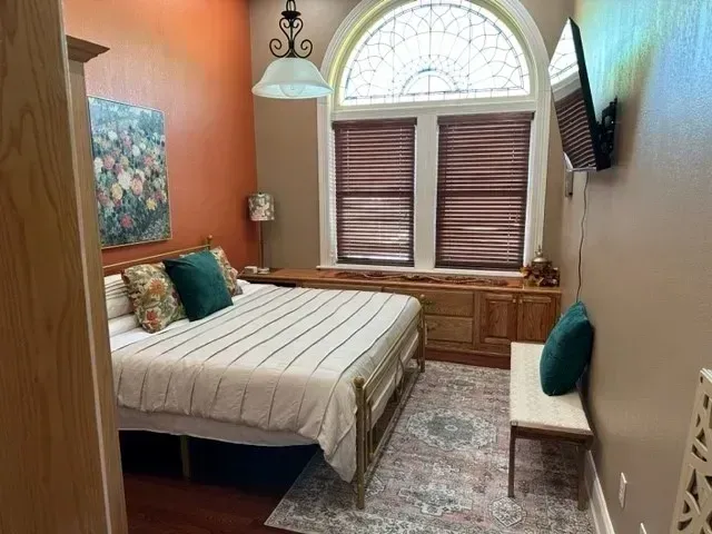 Small bedroom with a bed, window seat, patterned rug, and warm orange walls