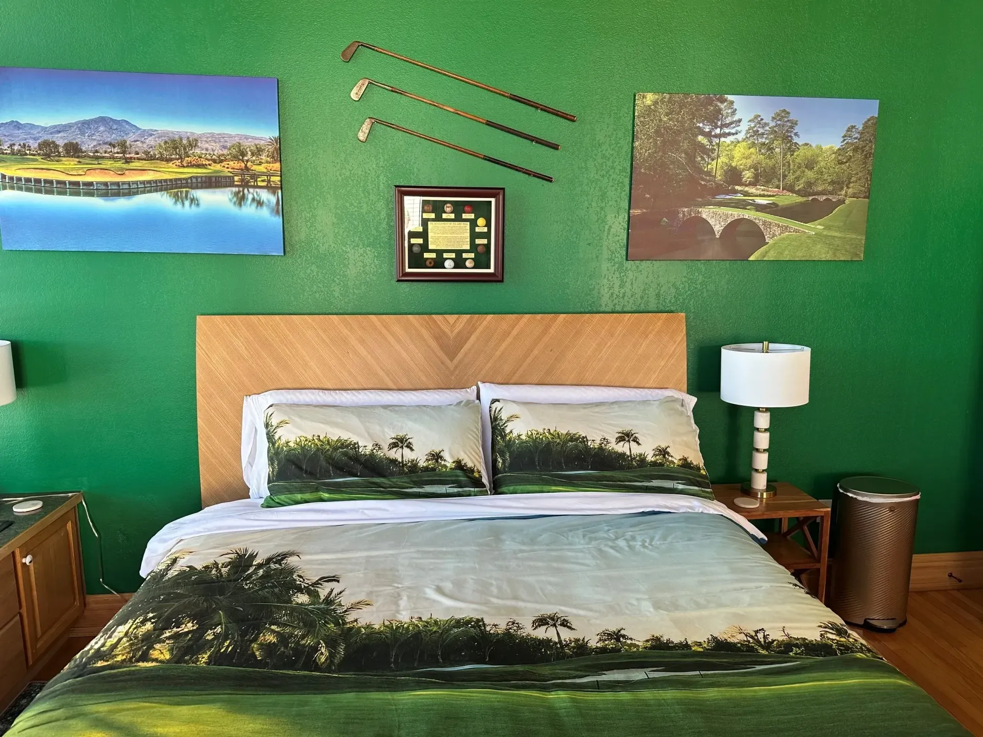 Bedroom with green walls, landscape art, and a bed with forest-print bedding and pillows