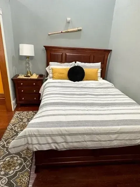Small bedroom with a wooden bed, striped bedding, bedside table, lamp, and patterned rug