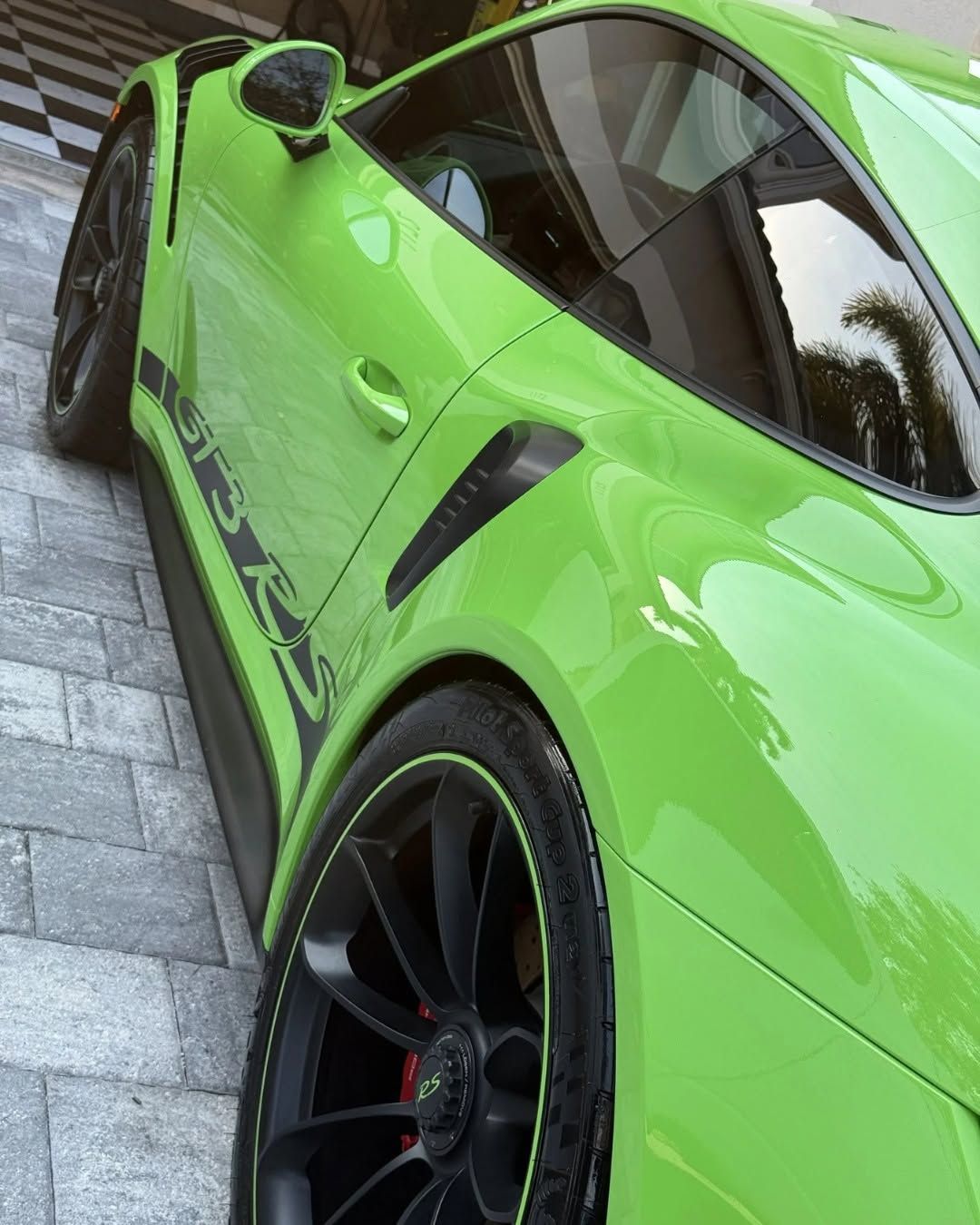 Bright green sports car with black wheels, parked on a stone driveway, viewed from the side.