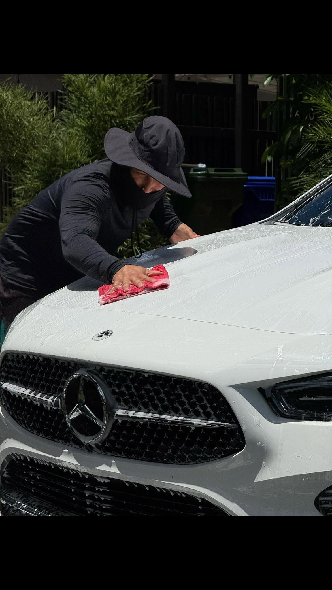 Person hand-washing a white Mercedes with a red cloth outdoors in daylight