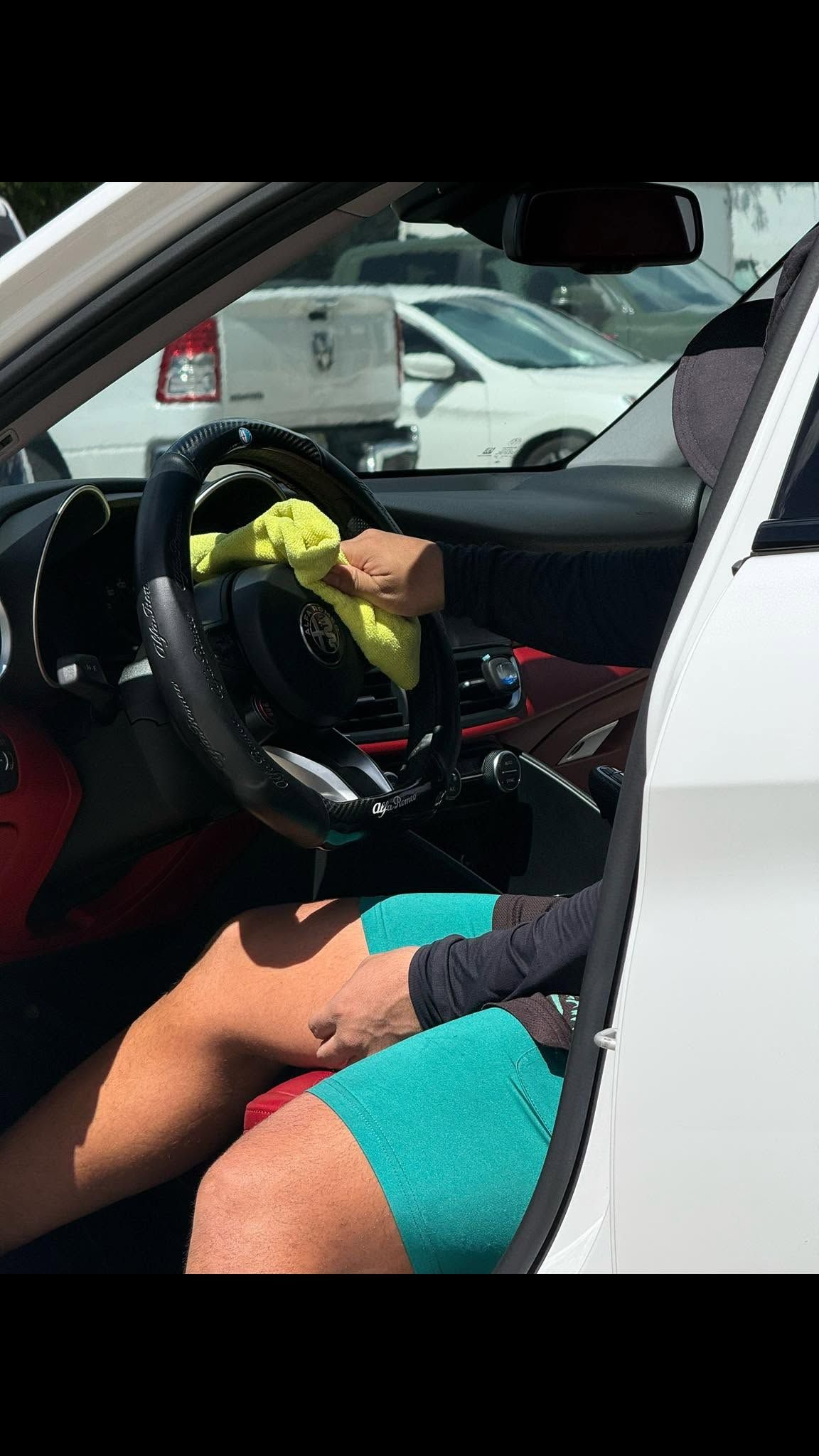 Person sitting in a white car’s driver seat, hand on the steering wheel, with legs visible in teal shorts.