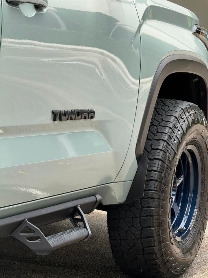 Close-up of a pale green Toyota truck’s side, showing off-road tire and side step.