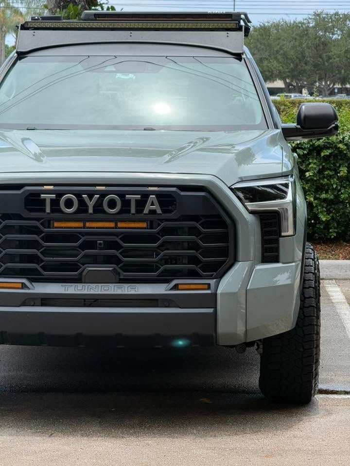 Front view of a gray Toyota SUV with off-road lights and roof rack, parked on a driveway.