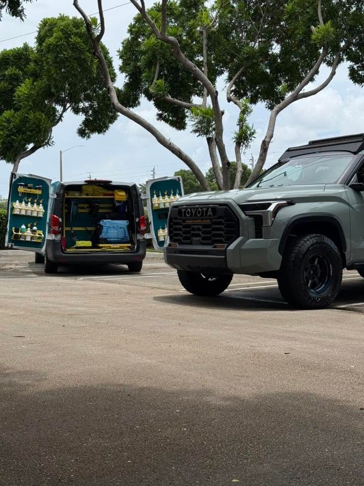 Two parked SUVs in a tree-lined lot, one green GWM front view and one dark van with colorful rear graphics.
