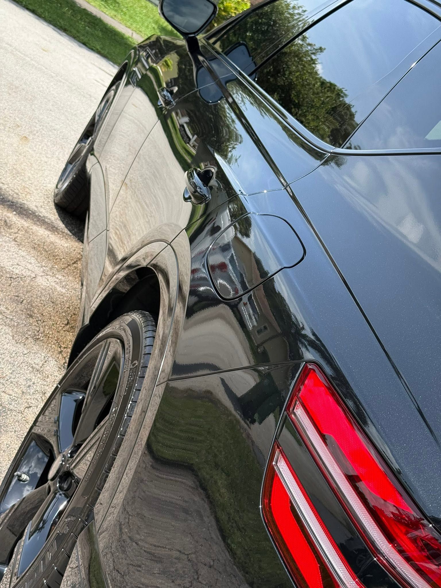 Black SUV parked on a driveway, showing the rear side and taillight in bright sunlight