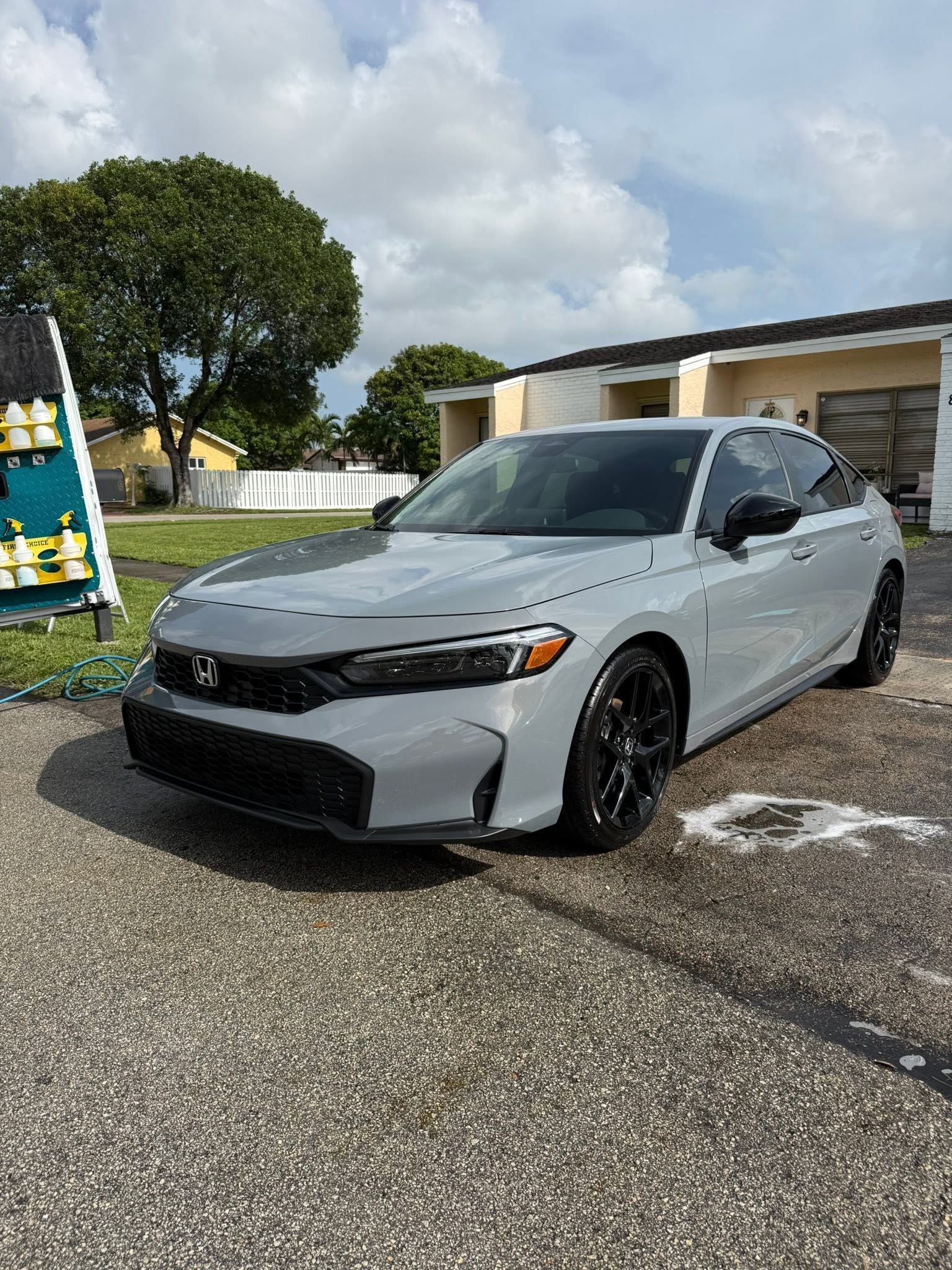 White sedan parked on wet pavement beside a building under a cloudy sky.