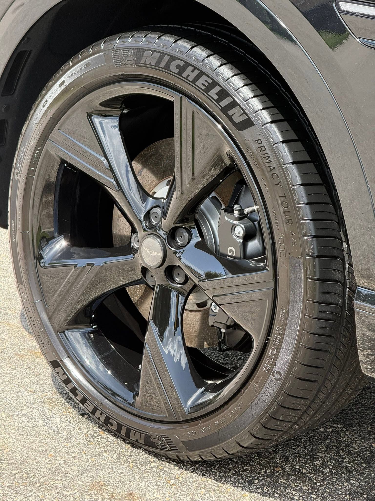 Close-up of a black car wheel with a shiny five-spoke rim and tire on pavement