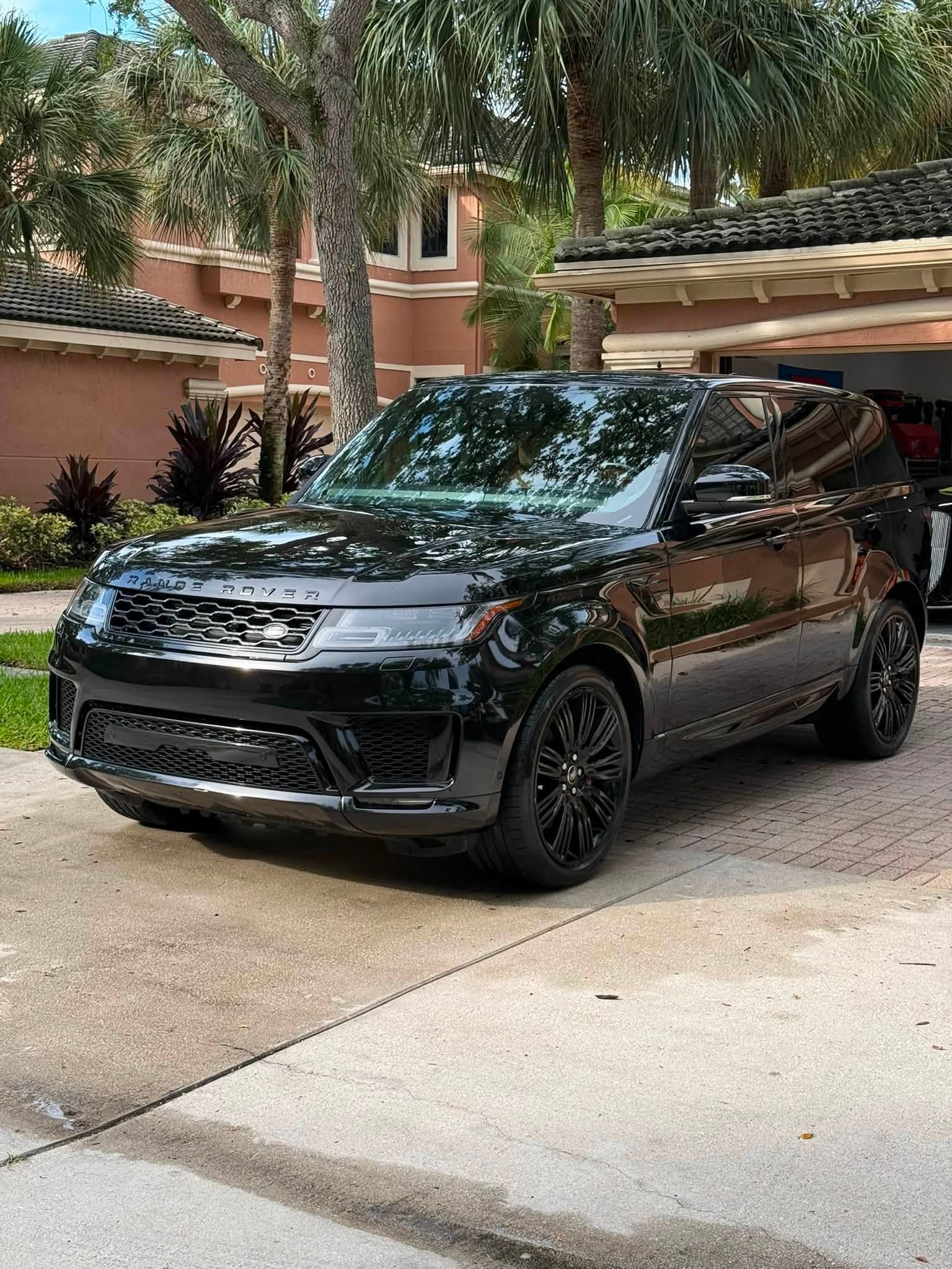 Black SUV parked in a driveway beside a house with trees and garage doors