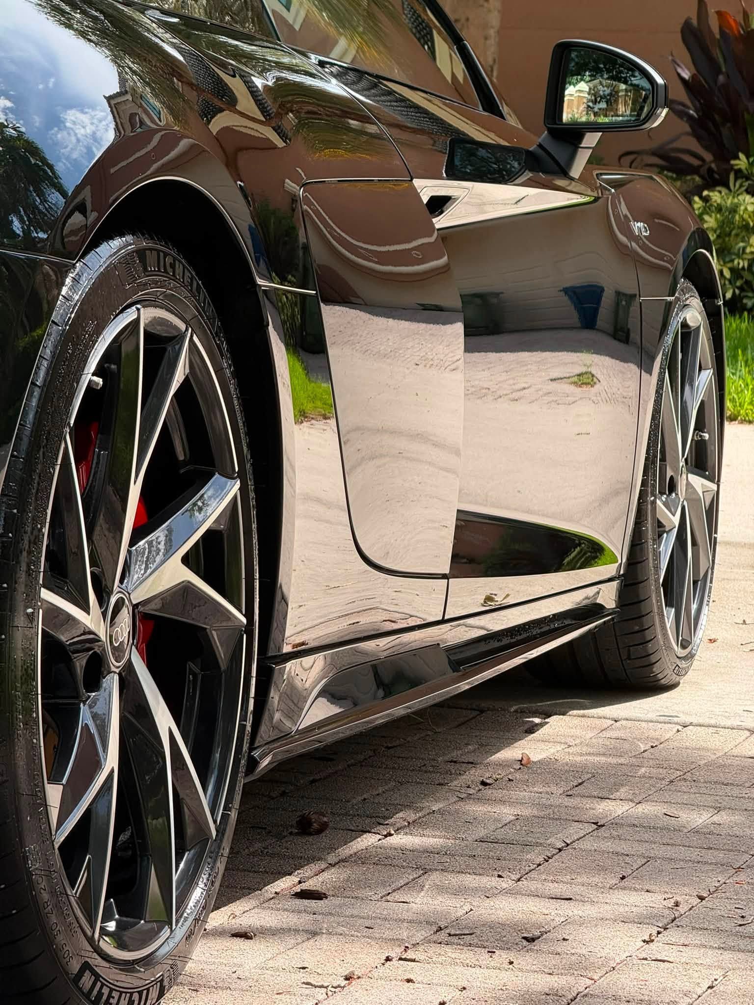 Glossy black sports car parked on a stone driveway, low-angle side view with wheels visible