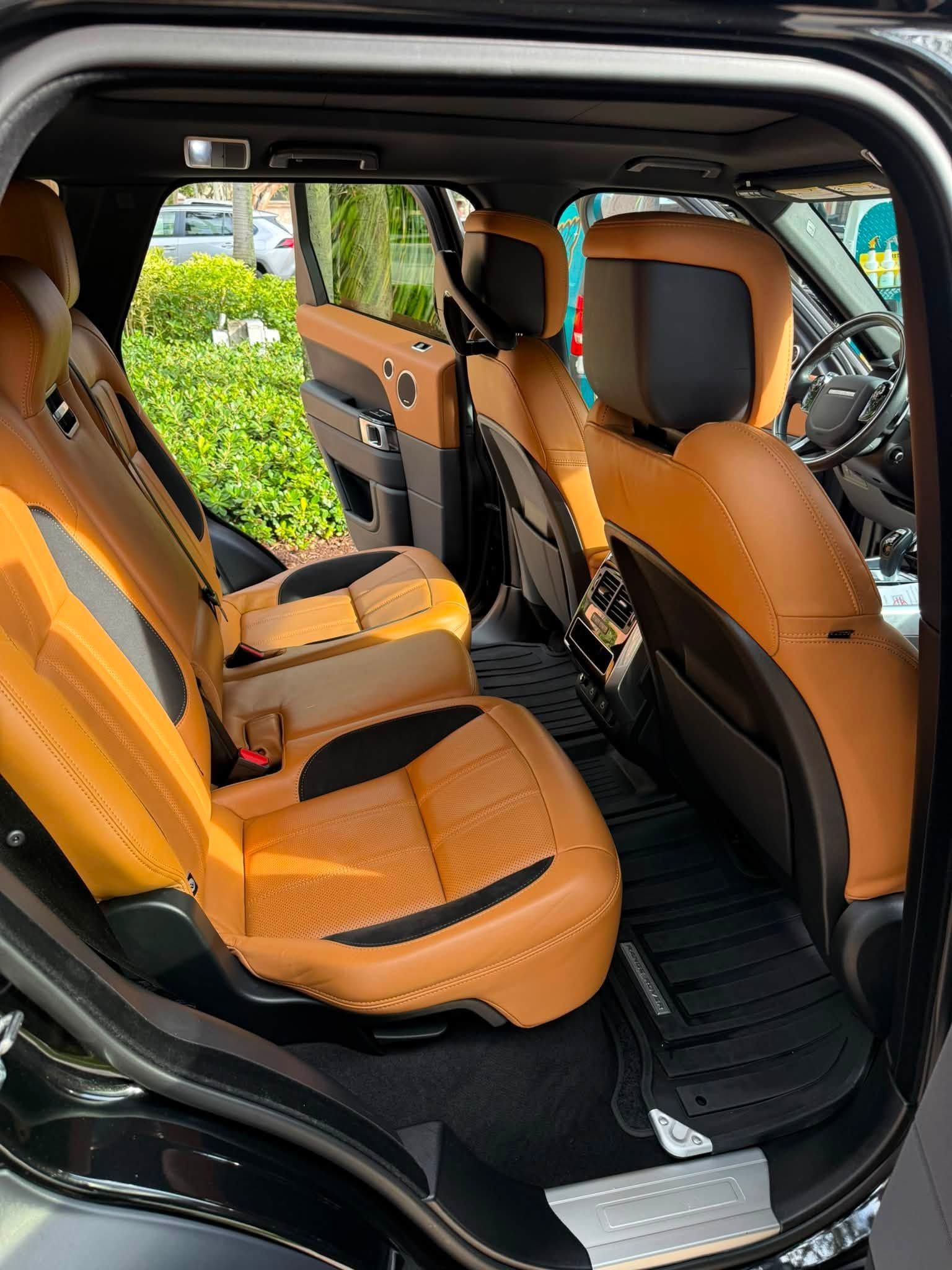 Black car interior with tan leather seats and open rear door, showing the back seat and front cabin.