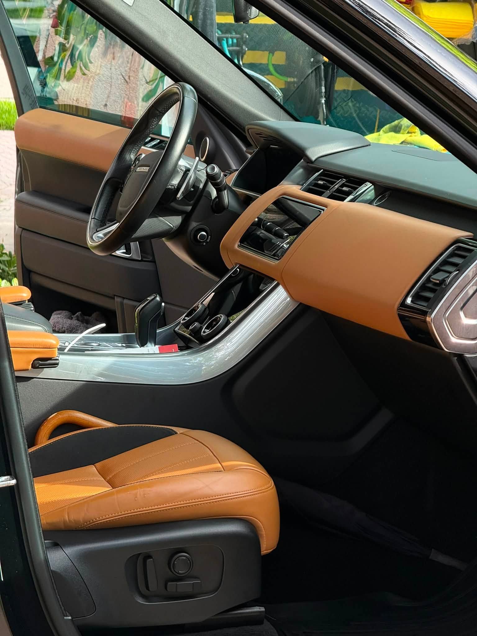 Car interior with tan leather seats, black dashboard, and steering wheel, viewed from the open passenger door