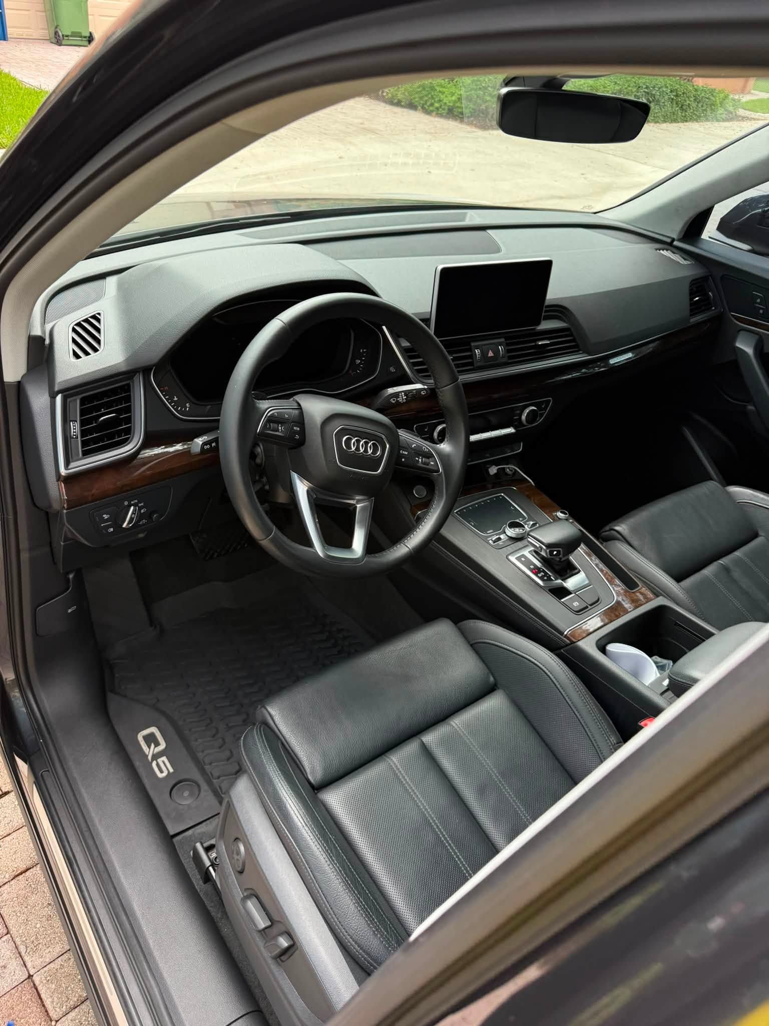 Car interior with black leather seats, steering wheel, and center console, viewed from the open driver’s door