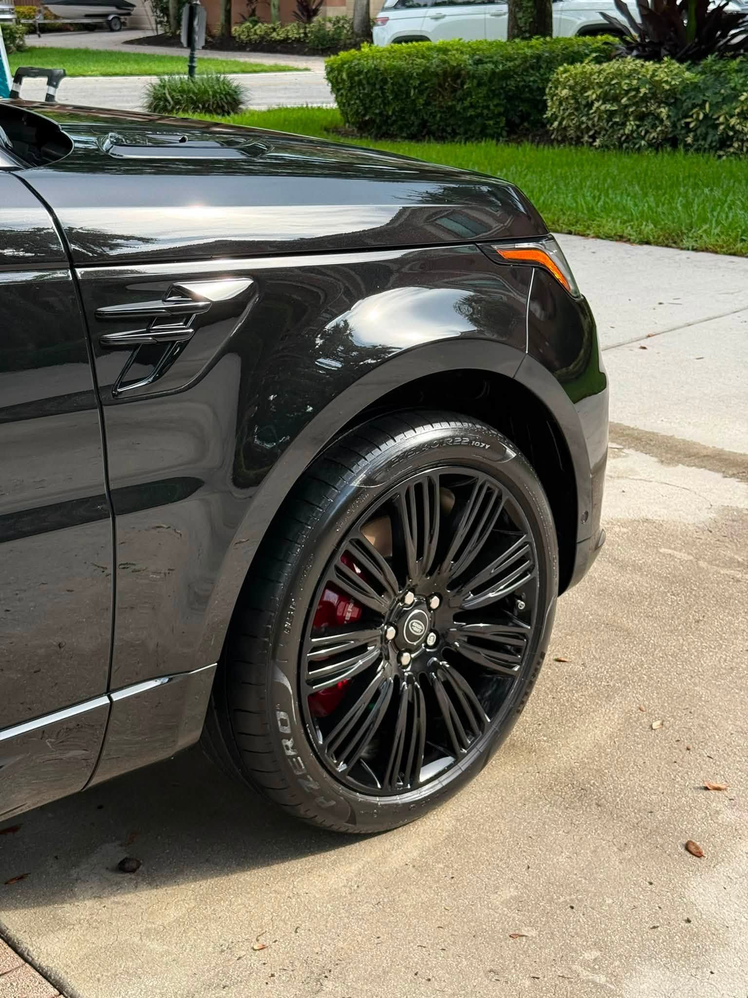Close-up of a black car’s front wheel and fender parked on a driveway.