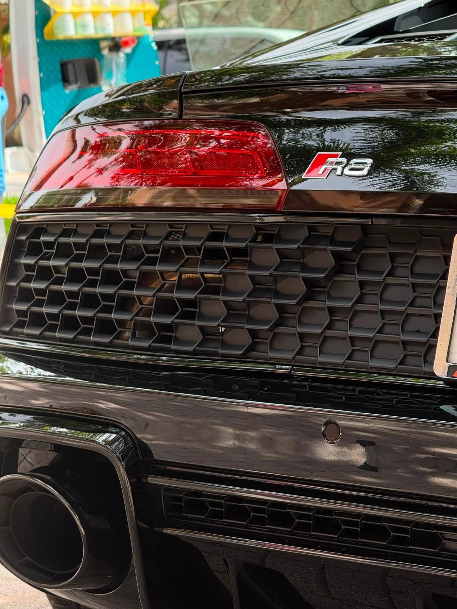 Close-up of a black sports car rear with red taillight, honeycomb grille, and large exhaust tip.