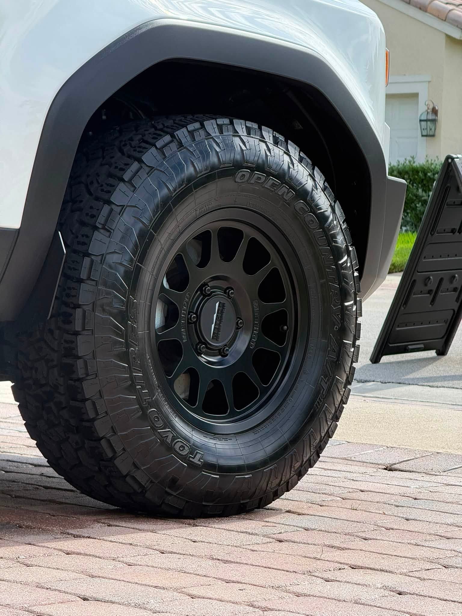 Black off-road tire and wheel on a silver vehicle parked on a brick driveway