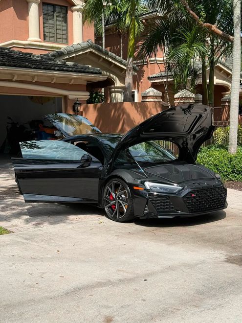Black sports car with open doors parked on a sunny street in front of a house.