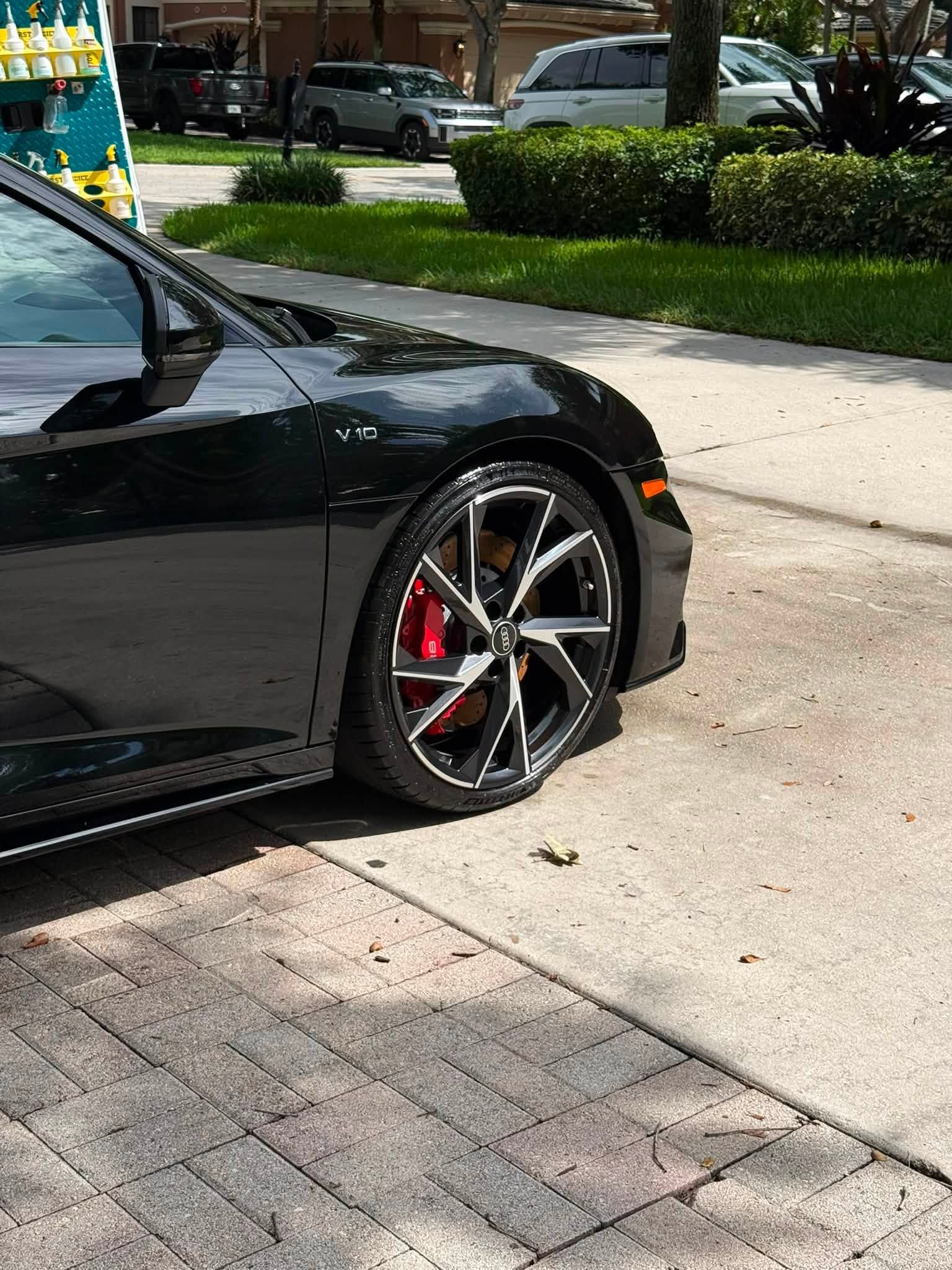 Black sports car parked by a curb, showing its front wheel and red brake caliper.