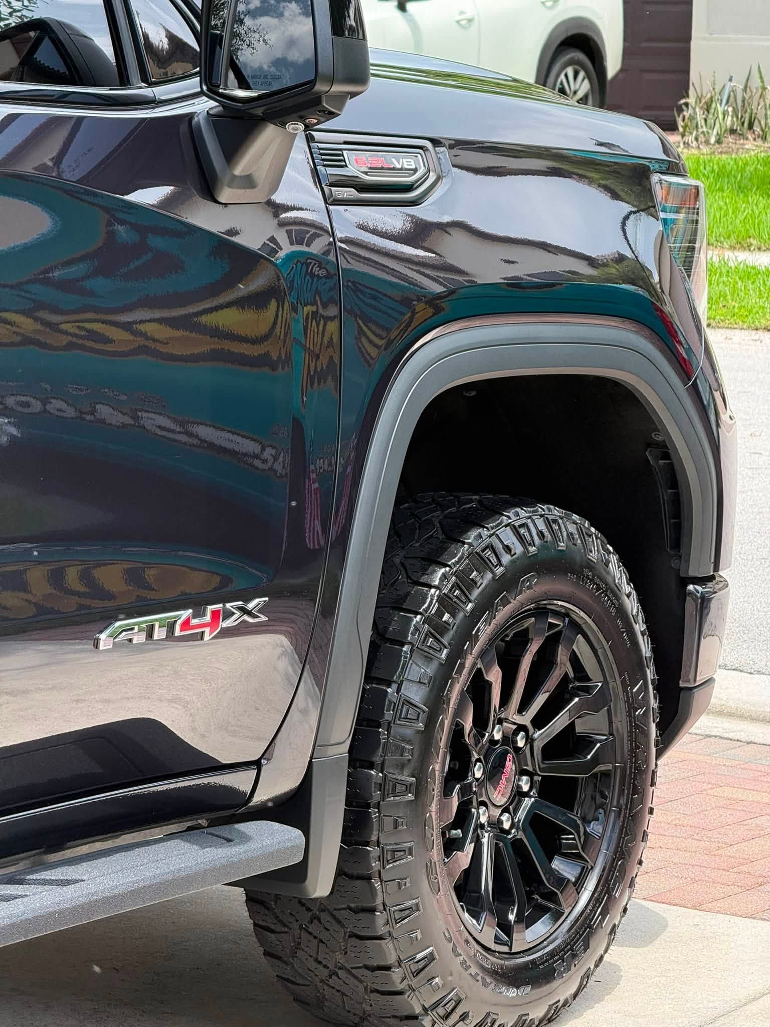 Close-up of a black GMC Sierra AT4 wheel and front fender with rugged tire on a driveway