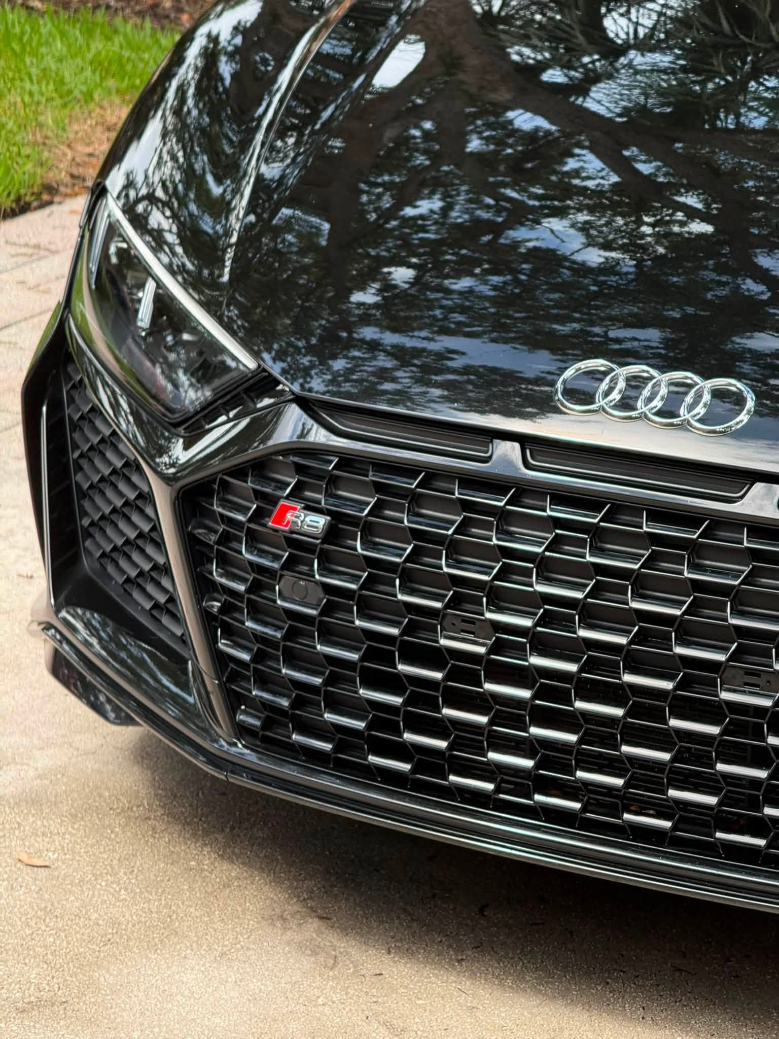 Close-up of a black Audi front grille with silver rings and red S badge parked on a driveway