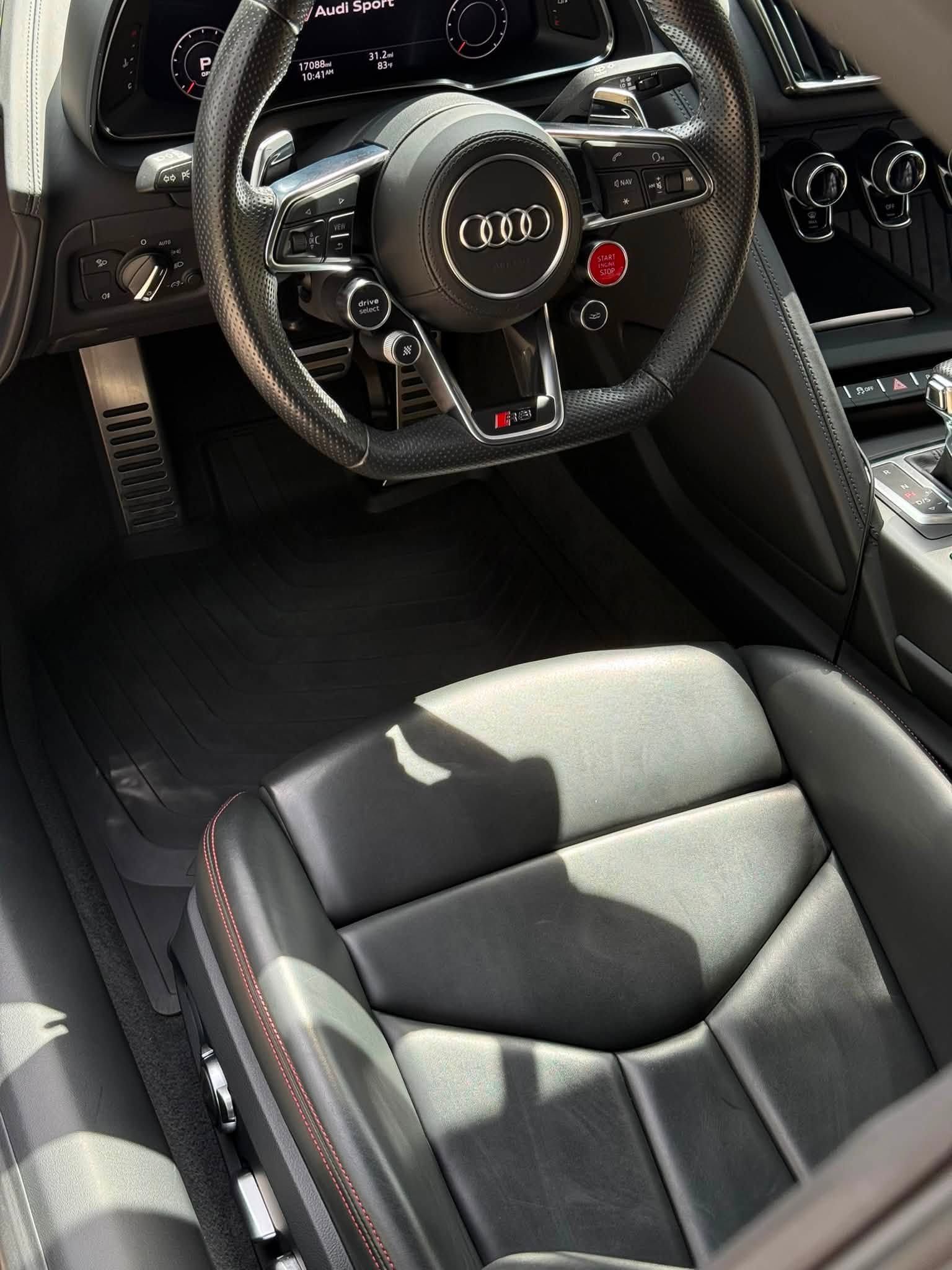 Black leather Audi interior with steering wheel and front seat visible, sunlight streaming in.