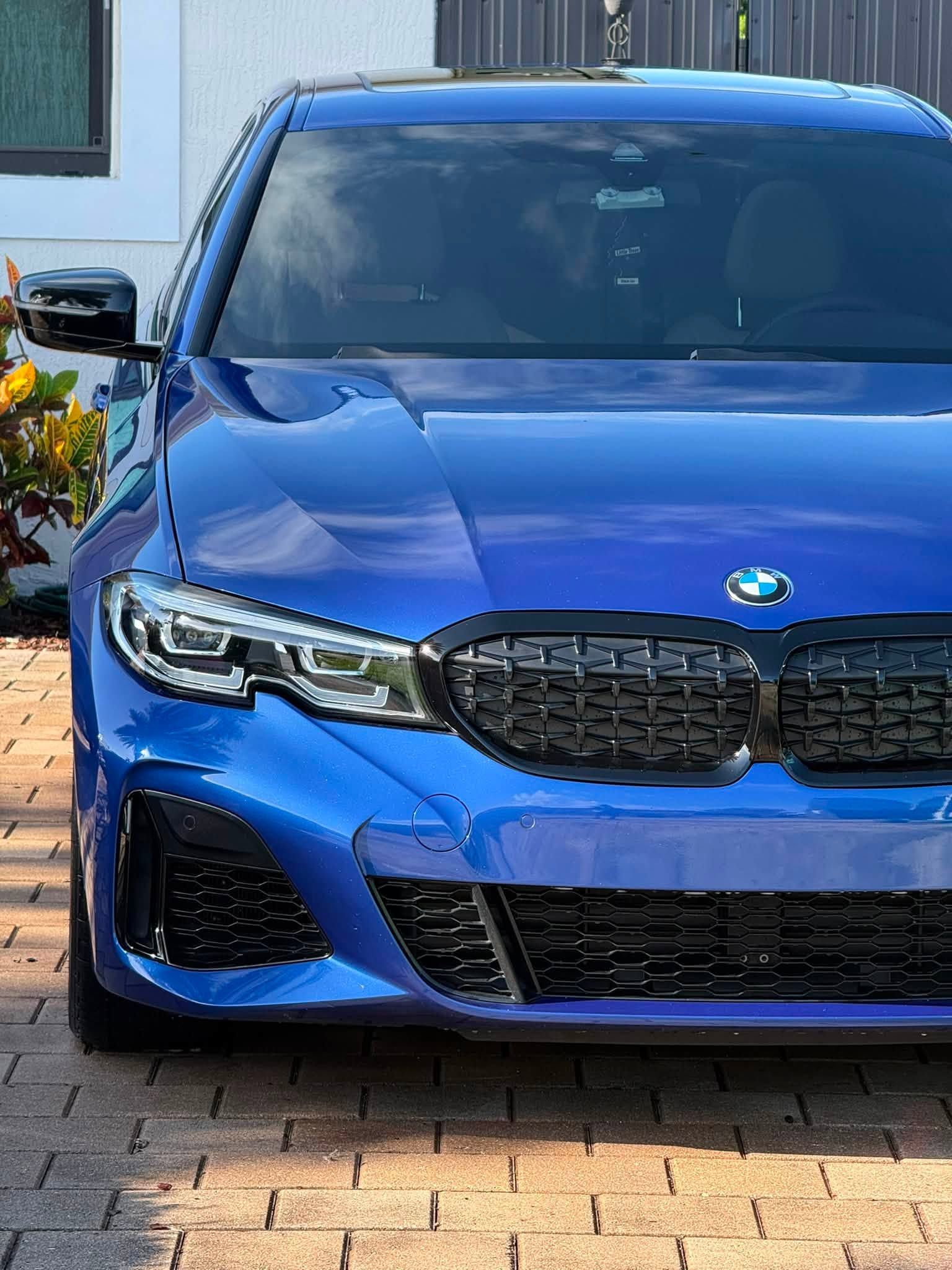 Front view of a blue BMW parked on a brick driveway beside a building.