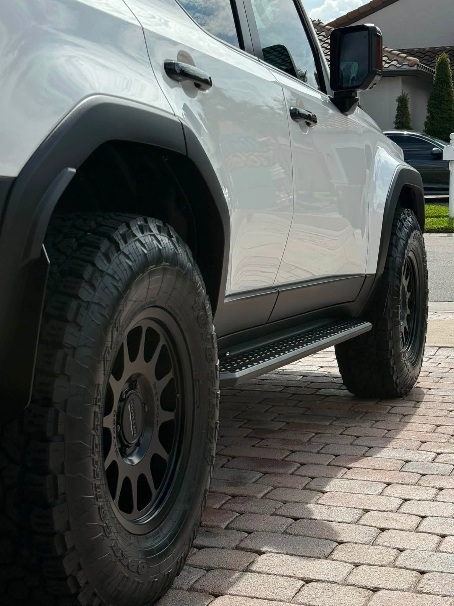 White off-road SUV with black wheels parked on a brick driveway