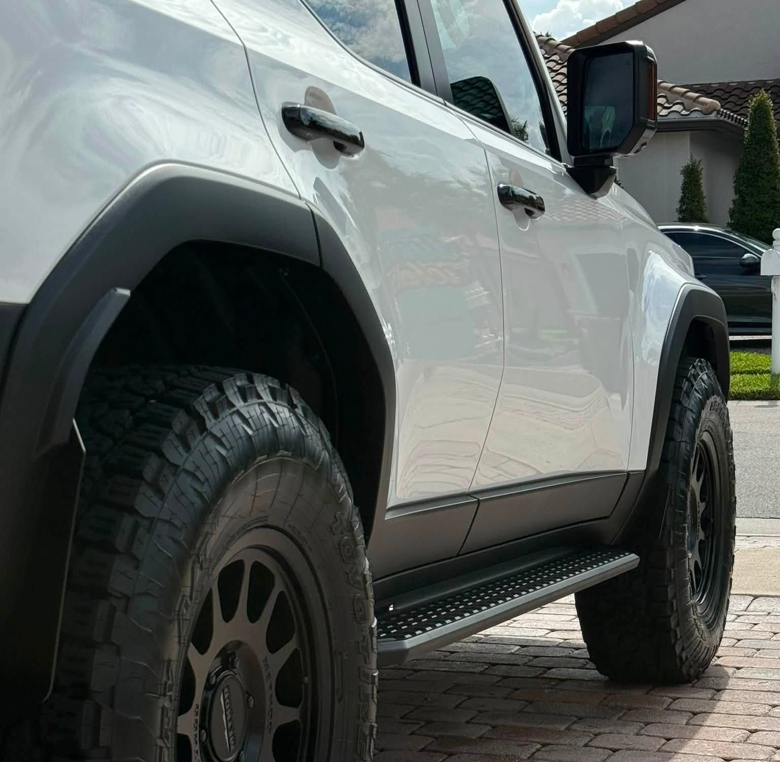 White off-road SUV with large tires parked in a driveway, viewed from the side.