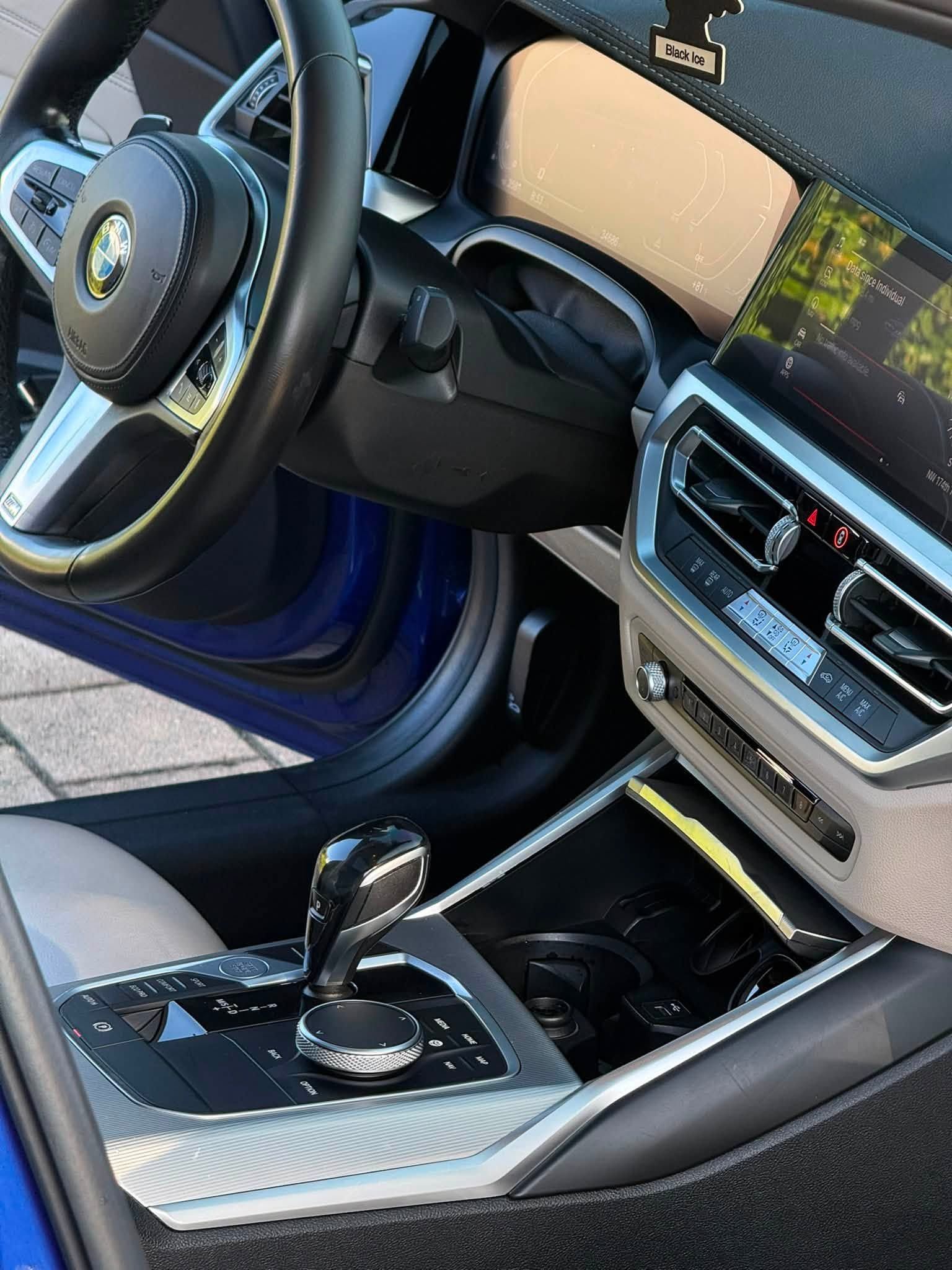 Luxury car interior with black leather seats, steering wheel, and center console, door open to the outside