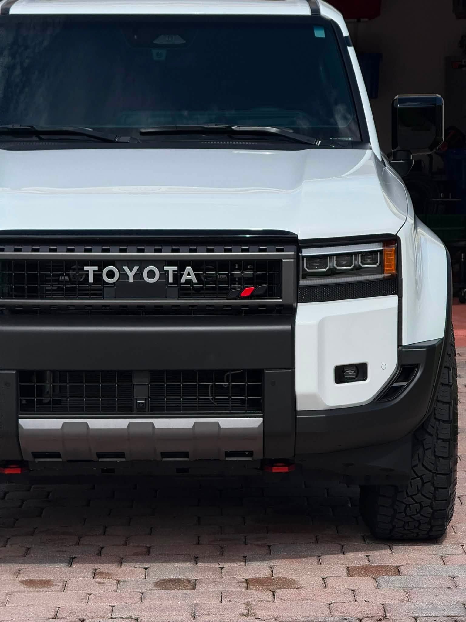 White Toyota off-road truck parked in a driveway, front view with black grille and rugged tires
