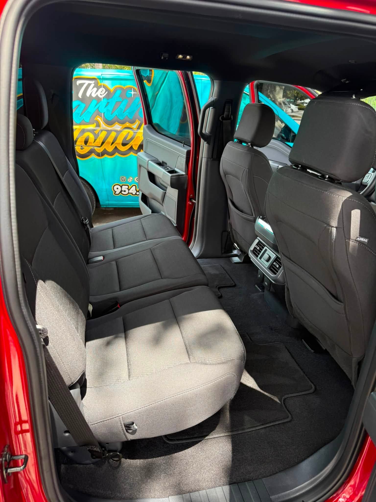 Open car door revealing a gray rear bench seat and black interior, with a turquoise sign visible outside.