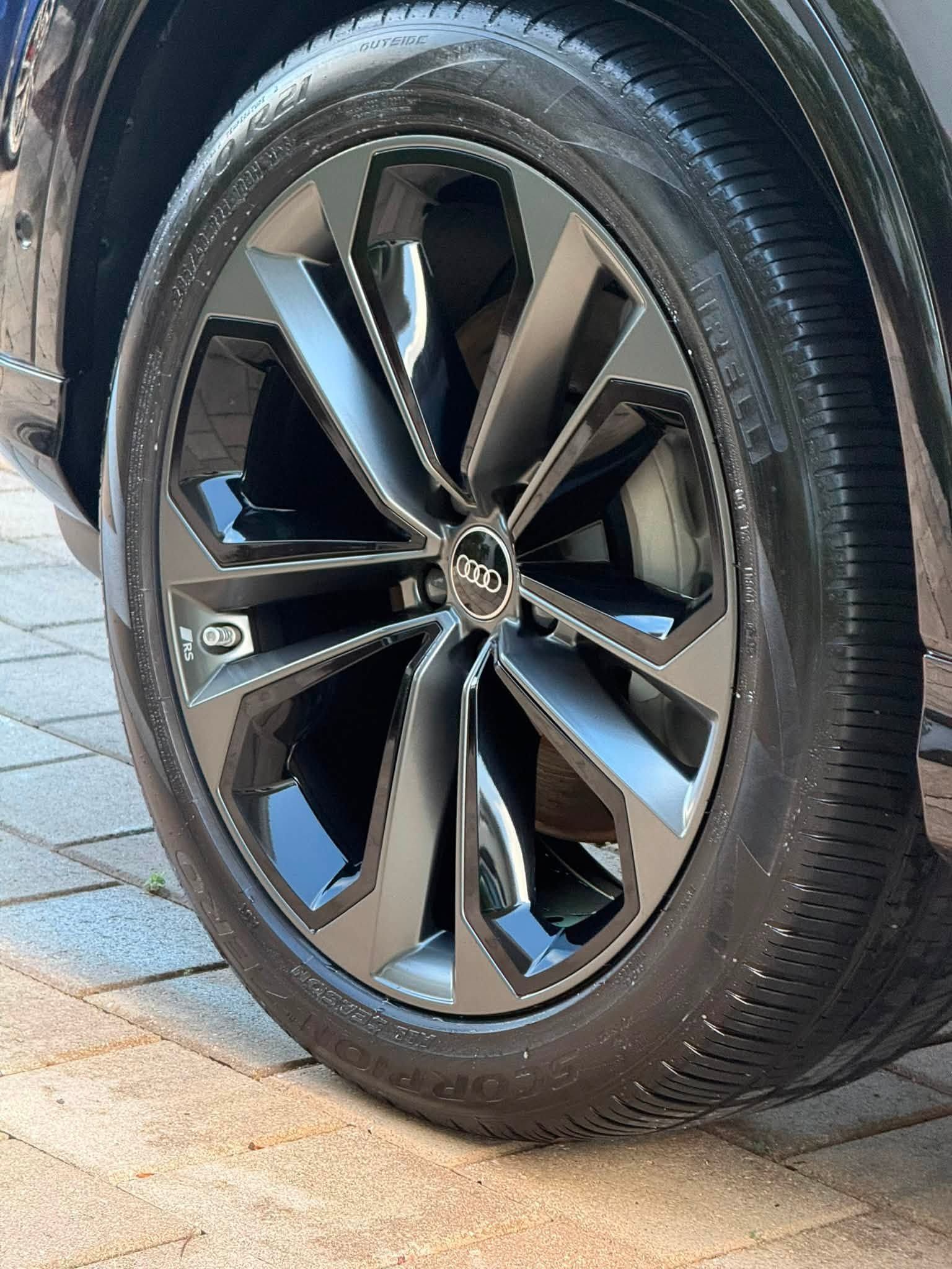 Close-up of a black alloy car wheel with silver accents and tire on a paved driveway