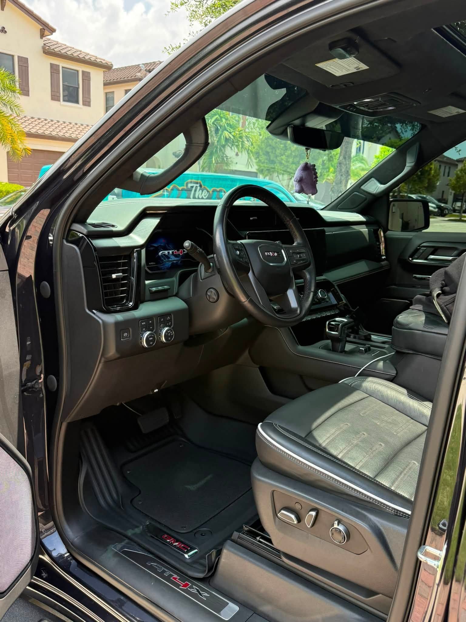 Open car door showing black leather interior, steering wheel, dashboard, and front seat controls.