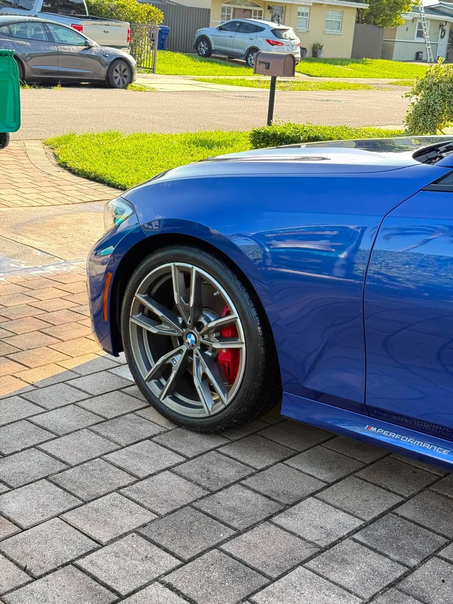 Blue sports car parked on a paved driveway, showing the front wheel and side panel.