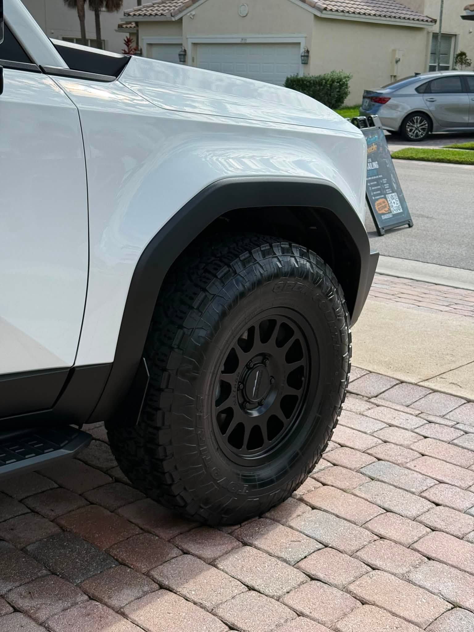White off-road vehicle with black wheel parked on a brick driveway in a suburban neighborhood