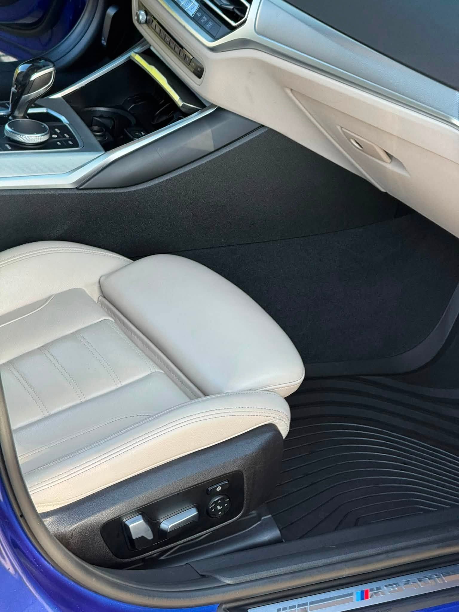 Front car passenger seat and footwell with beige leather, black dashboard trim, and floor mat