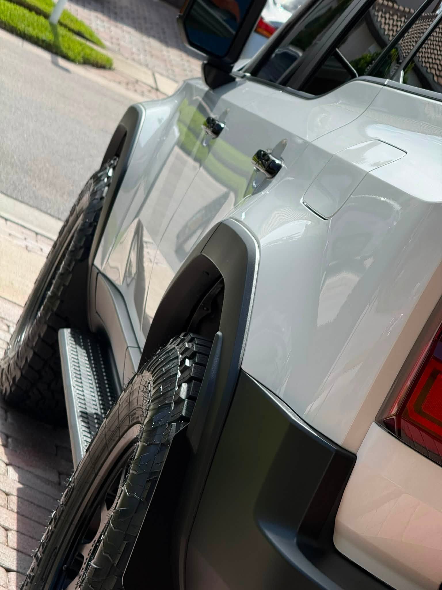 White SUV parked at a curb, shown from the rear side with large off-road tires and black trim.