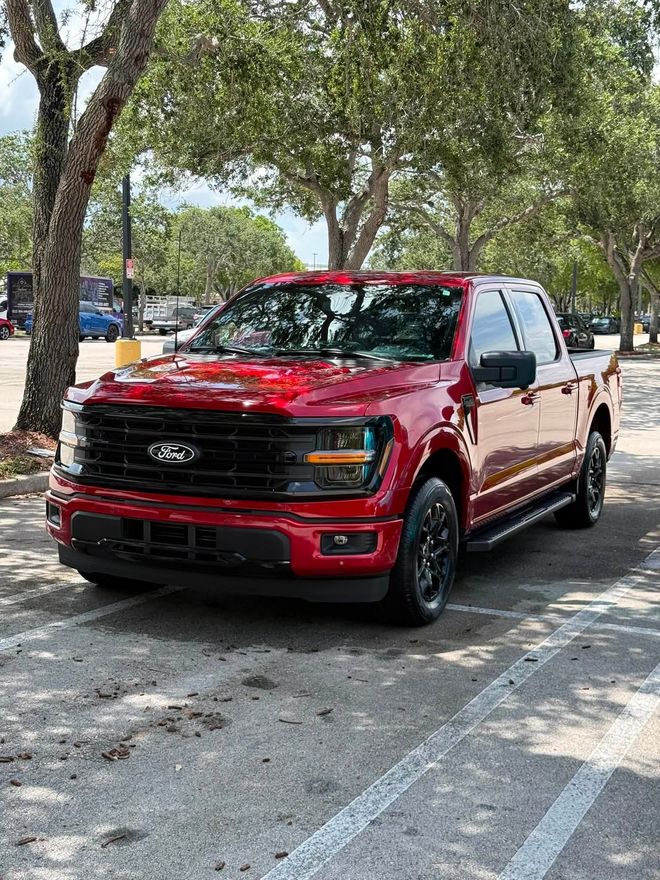 Red pickup truck parked under trees along a sunny street