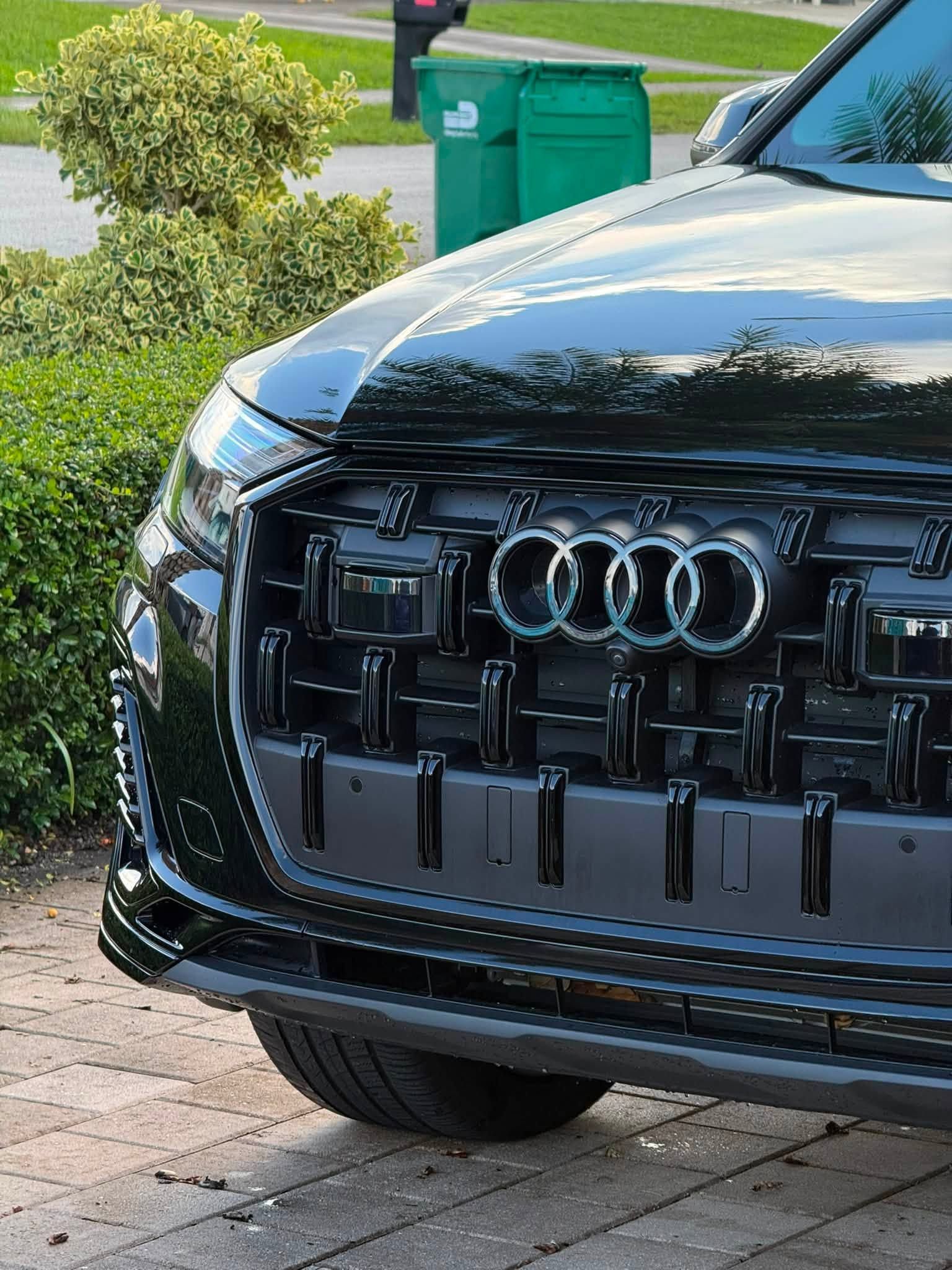 Black Audi SUV front grille parked on a driveway with greenery in the background