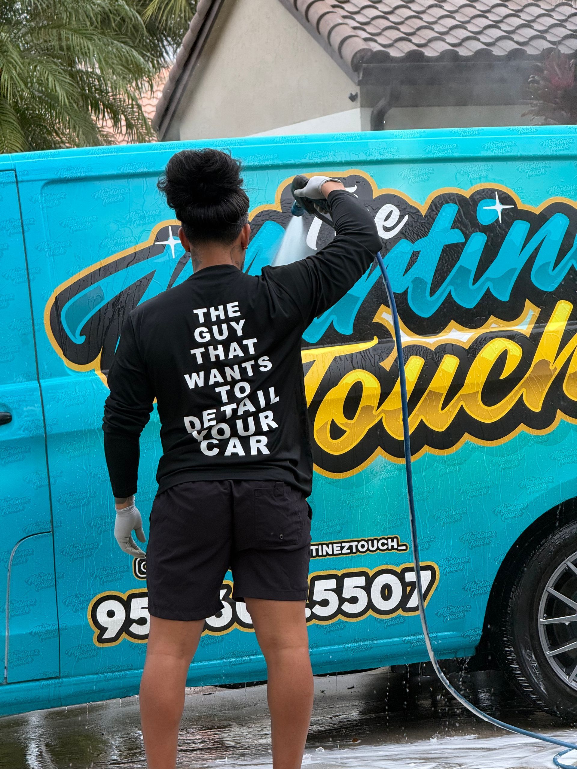 Man spray-painting turquoise car wrap with bold yellow lettering in a driveway